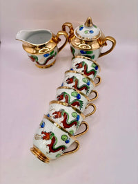 Decorative tea set with cups, teapot, and creamer featuring dragon designs on a light pink background.