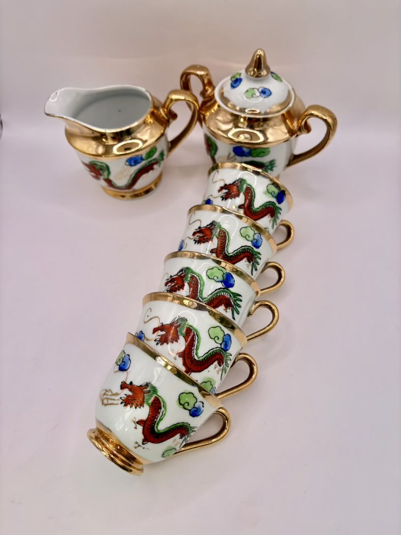 Decorative tea set with cups, teapot, and creamer featuring dragon designs on a light pink background.