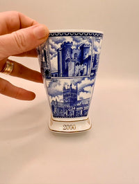 Ceramic cup with blue architectural design held by a hand on a beige background