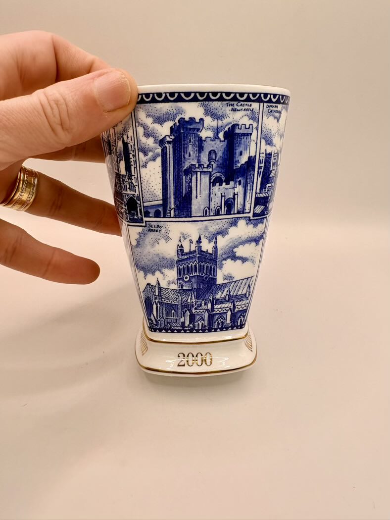 Ceramic cup with blue architectural design held by a hand on a beige background
