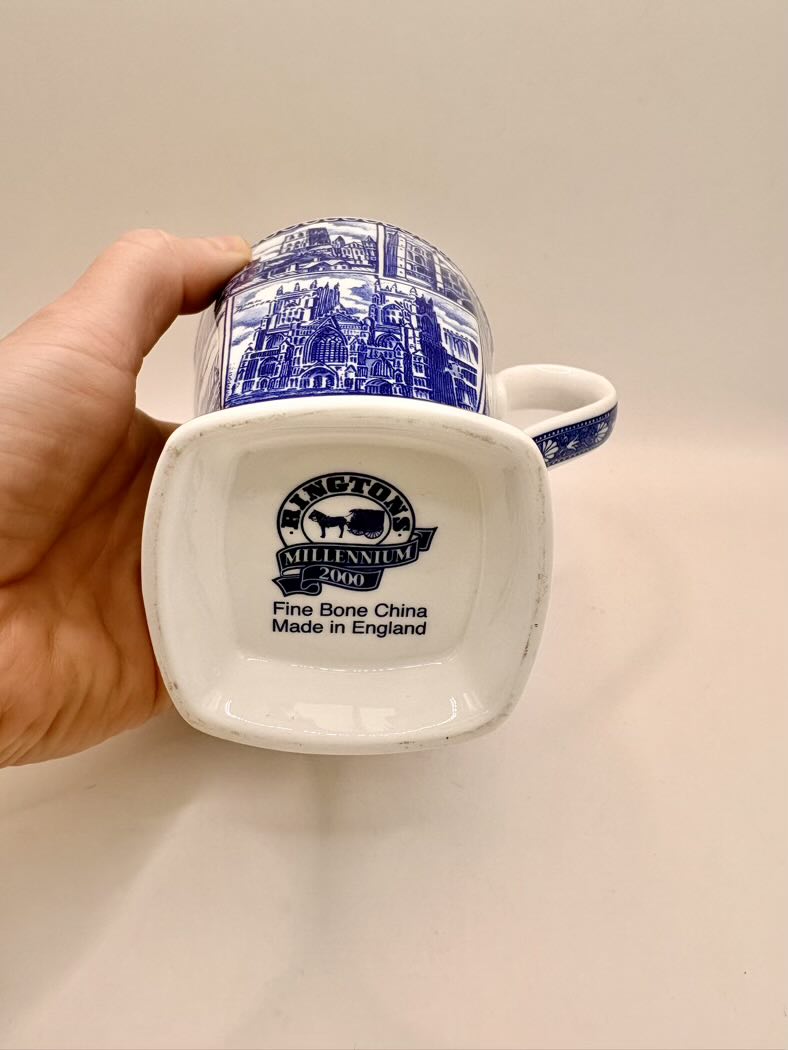 White mug with blue decorative patterns held by a hand on a beige background