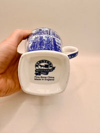 White mug with blue decorative patterns held by a hand on a beige background