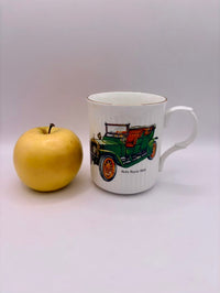 Mug with vintage car design next to an apple on a white background