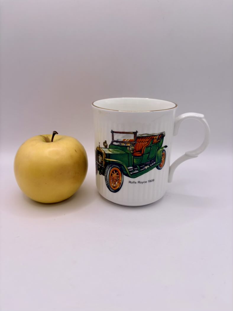 Mug with vintage car design next to an apple on a white background