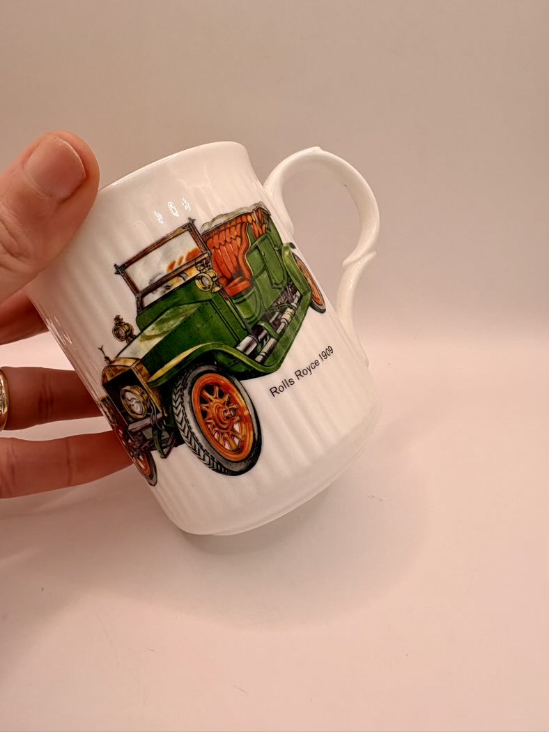 White mug with a green car design held by a hand on a light background