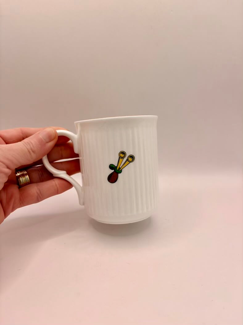 White mug with a colorful design held by a hand on a light pink background