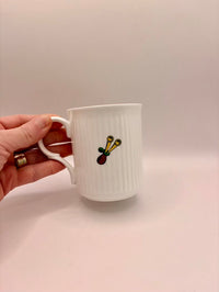 White mug with a colorful design held by a hand on a light pink background