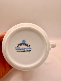 Close-up of a white ceramic cup with 'Sadler Wellington' branding on a light background
