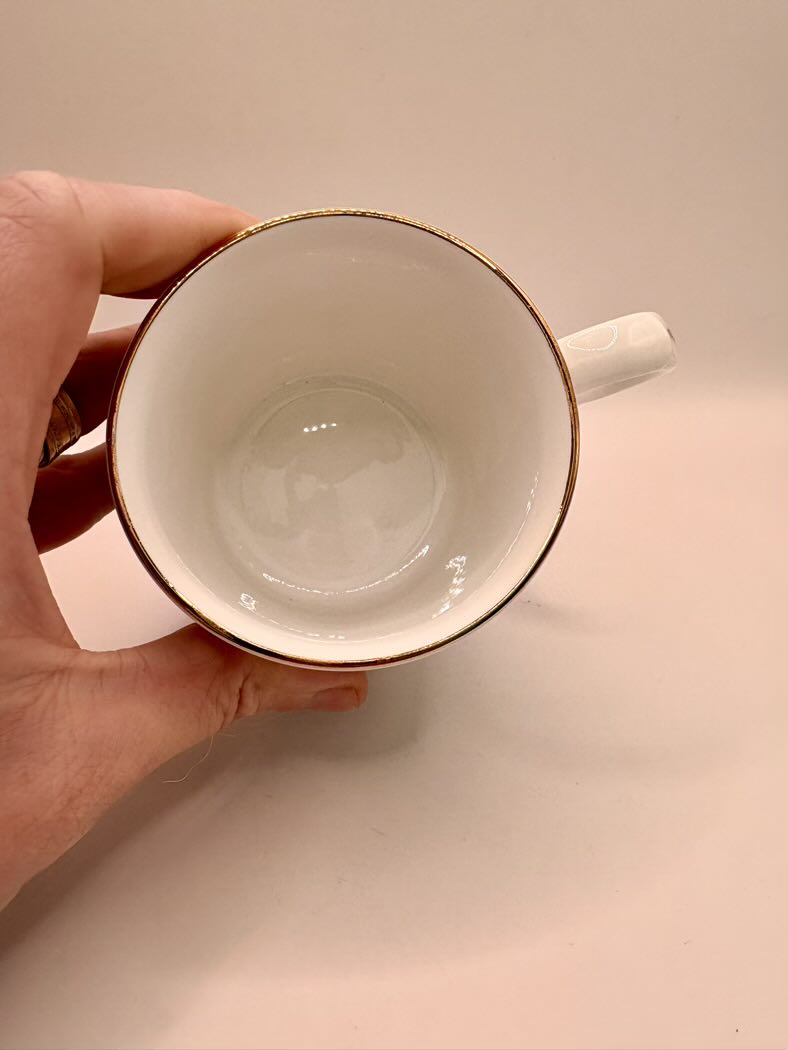 White mug with gold rim held by a hand on a beige background