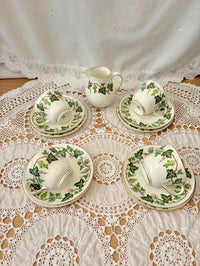 Set of white ceramic tea set with green leaf patterns on a lace tablecloth.
