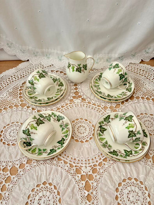 Set of white ceramic tea set with green leaf patterns on a lace tablecloth.