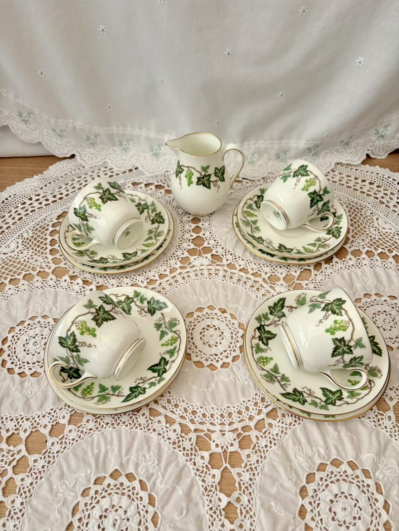 Set of white ceramic tea set with green leaf patterns on a lace tablecloth.