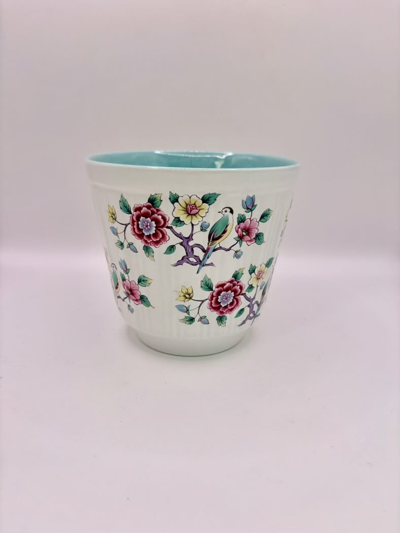 Ceramic cup with floral and bird design on a white background