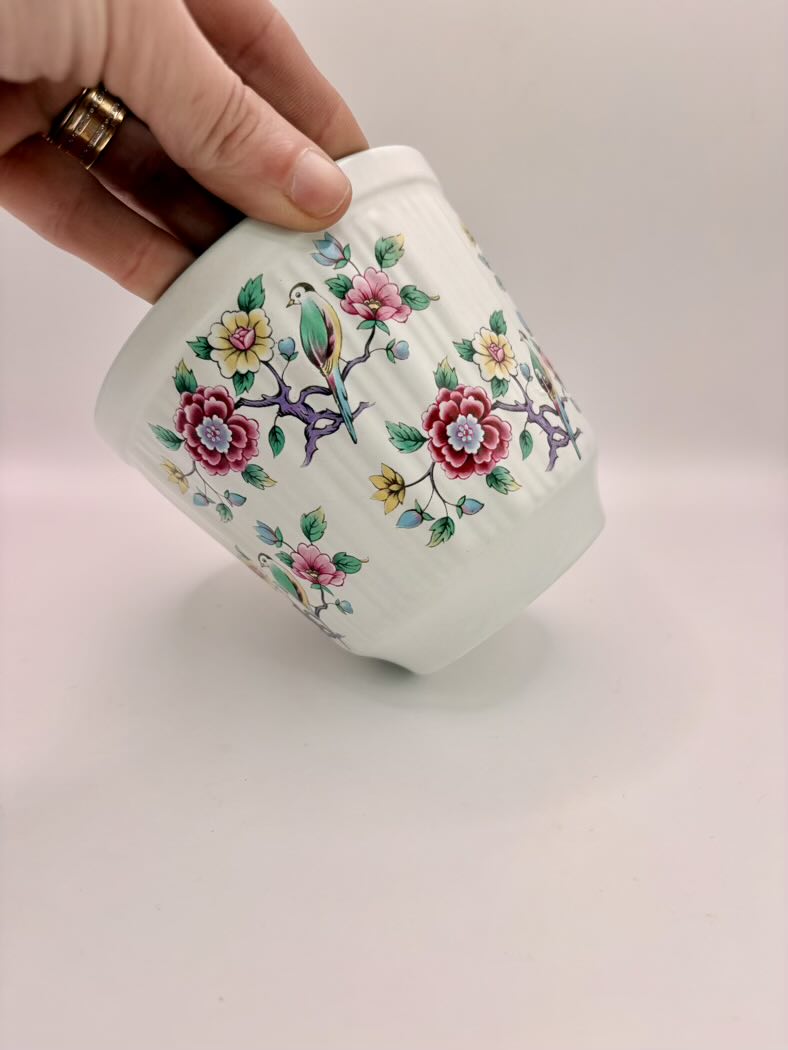 Hand holding a small ceramic container with floral designs on a light background