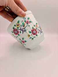 Hand holding a small ceramic container with floral designs on a light background