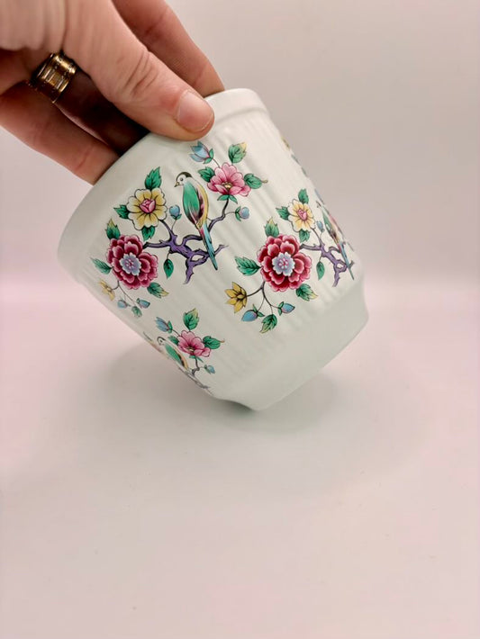 Hand holding a small ceramic container with floral designs on a light background