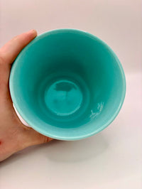 Hand holding a teal cup against a white background