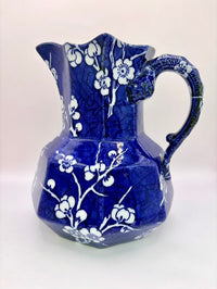Blue ceramic pitcher with white floral patterns on a white background