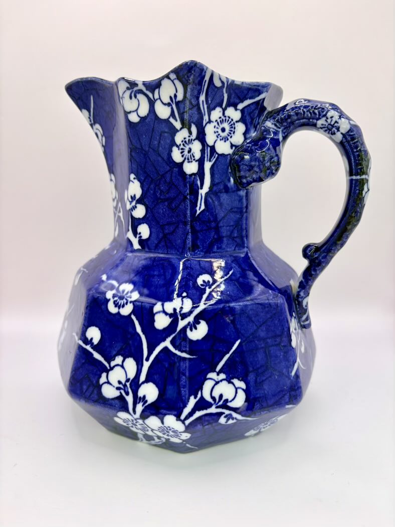 Blue ceramic pitcher with white floral patterns on a white background