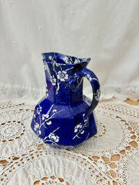 Blue ceramic pitcher with white floral patterns on a lace tablecloth