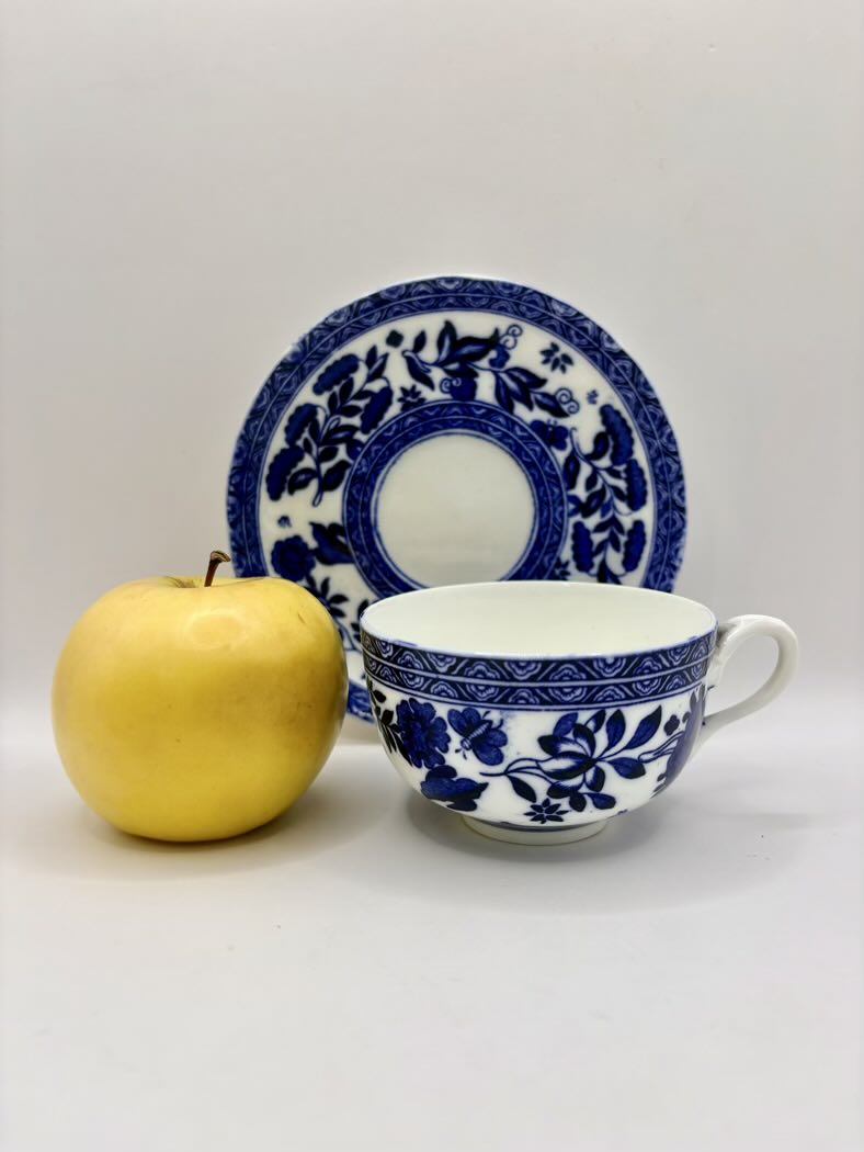 Blue and white teacup and saucer with a yellow apple on a light gray background