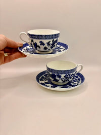 Two blue and white teacups with saucers on a beige surface.