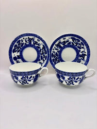 Two blue and white ceramic teacups with saucers on a light gray background