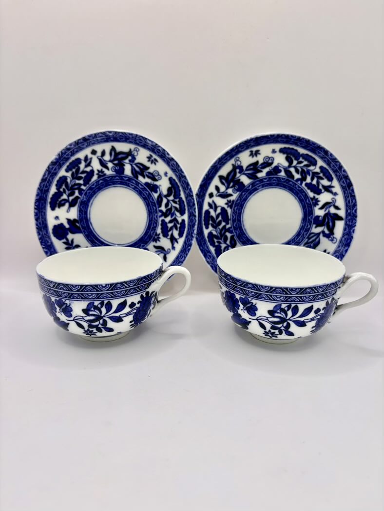 Two blue and white ceramic teacups with saucers on a light gray background