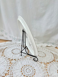 White plate on a black stand with a white lace tablecloth in the background