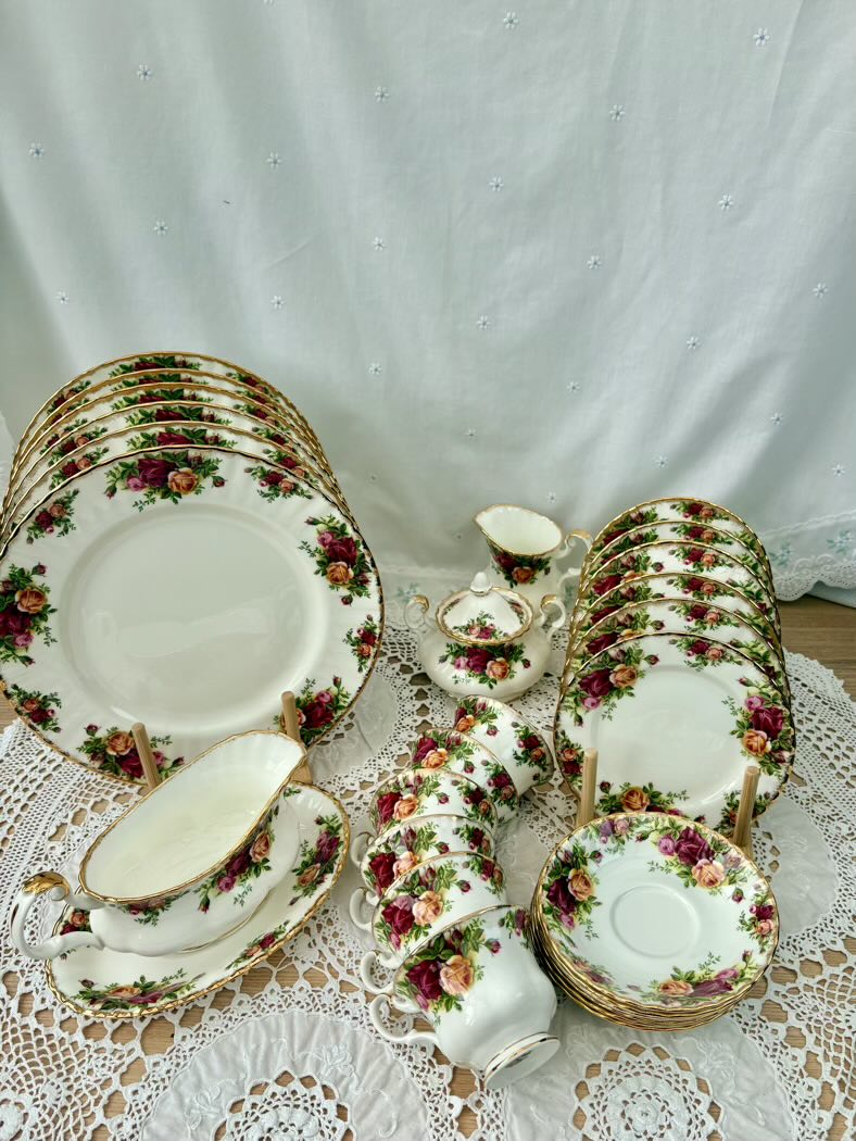 Set of floral-patterned ceramic dinnerware on a lace tablecloth with a white curtain background.