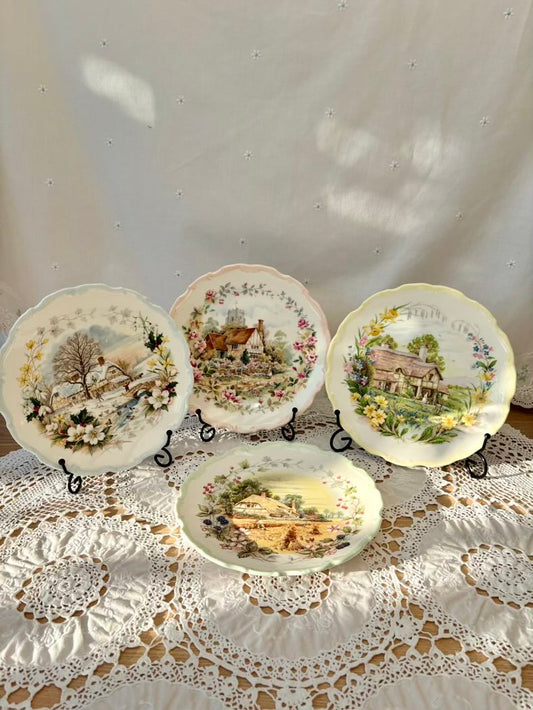 Set of decorative plates with scenic designs on a lace tablecloth.