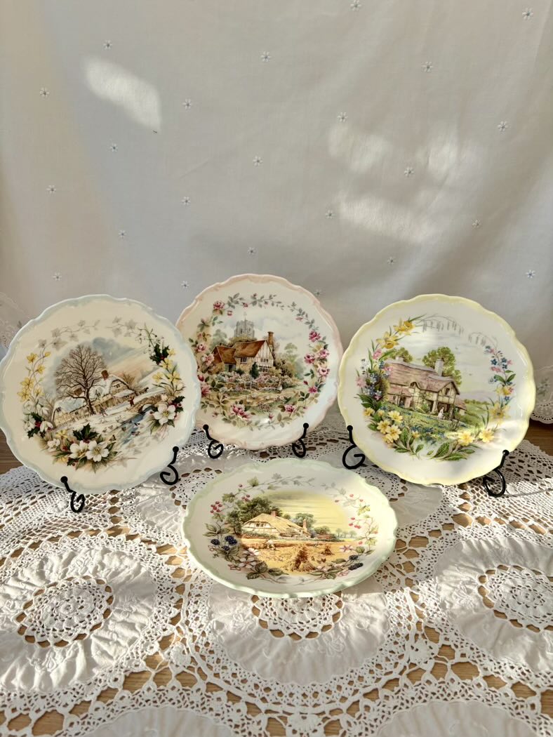 Set of decorative plates with scenic designs on a lace tablecloth.
