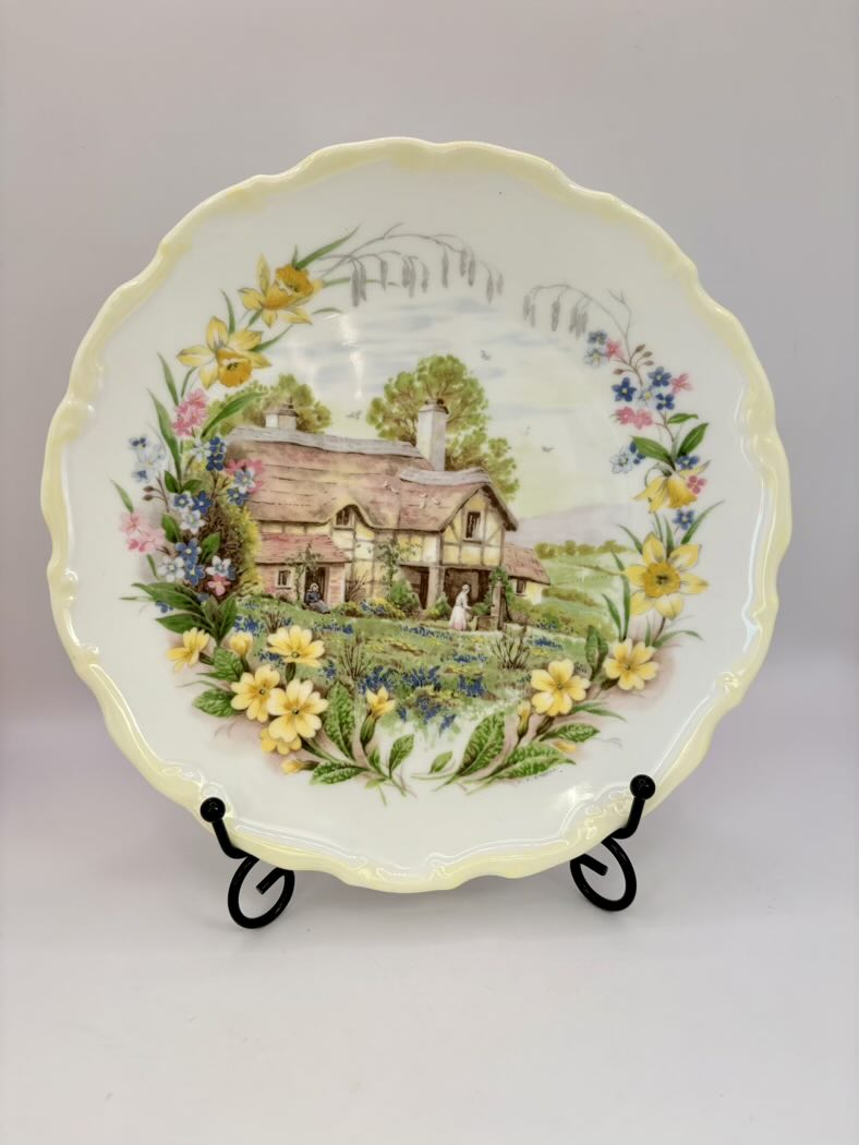 Decorative plate with a scenic design of a house and flowers on a stand against a gray background
