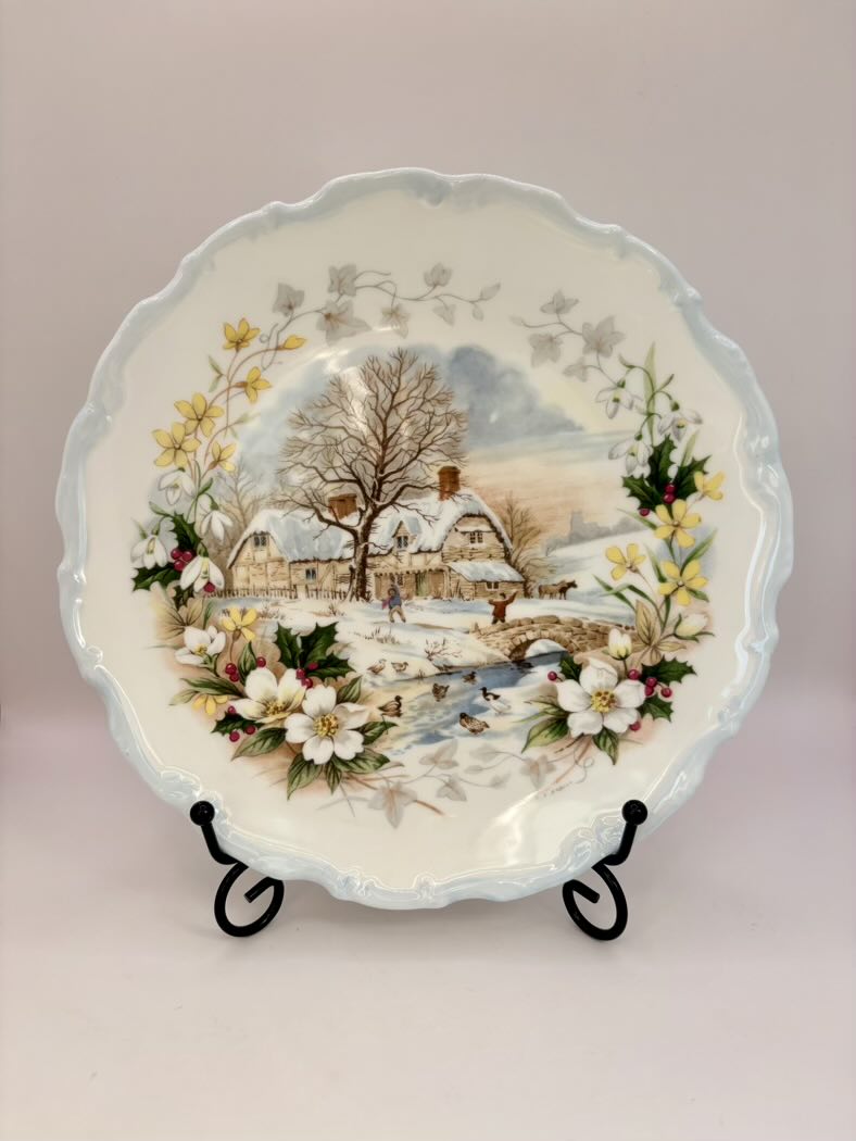 Decorative plate with a winter scene and floral elements on a stand against a light background