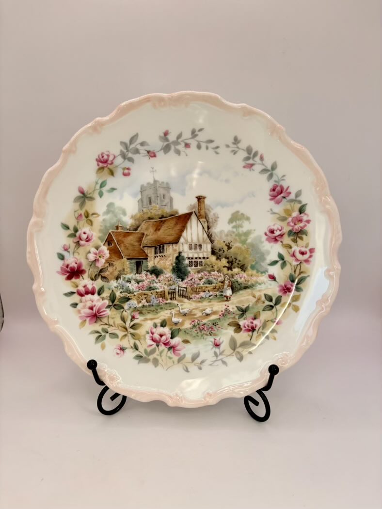 Decorative plate with a scenic design of a house and garden on a stand against a plain background