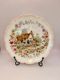 Decorative plate with a scenic design of a house and garden on a stand against a plain background