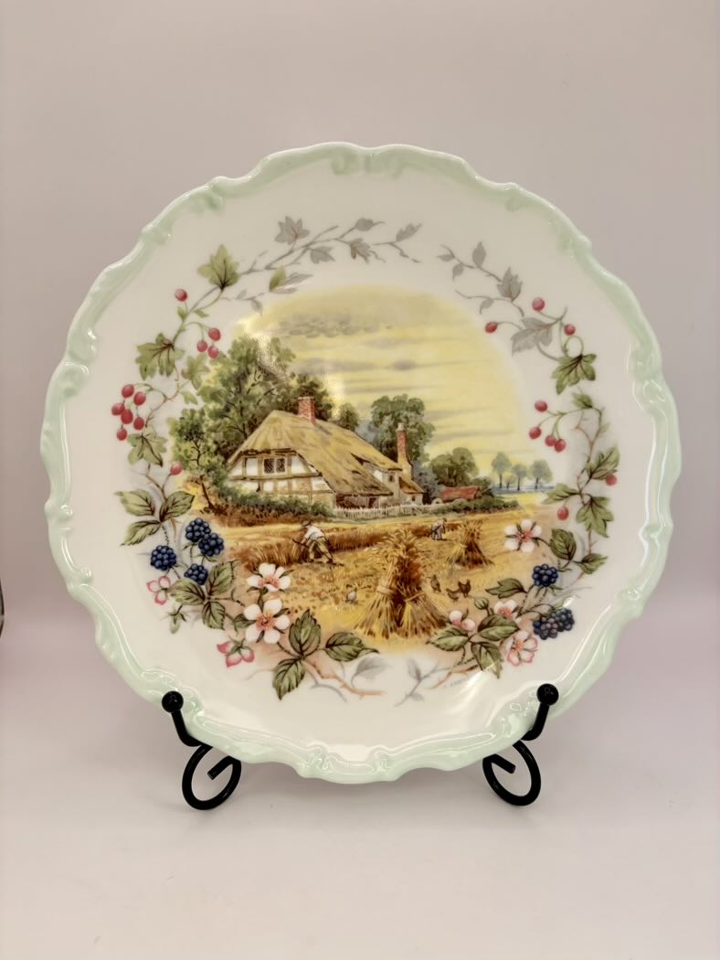 Decorative plate with a scenic design of a house and nature on a stand against a plain background.