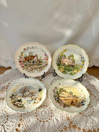 Four decorative plates with scenic designs on a lace tablecloth.