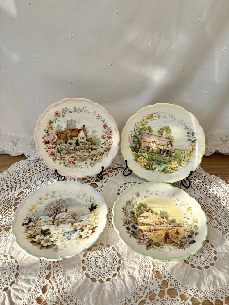 Four decorative plates with scenic designs on a lace tablecloth.