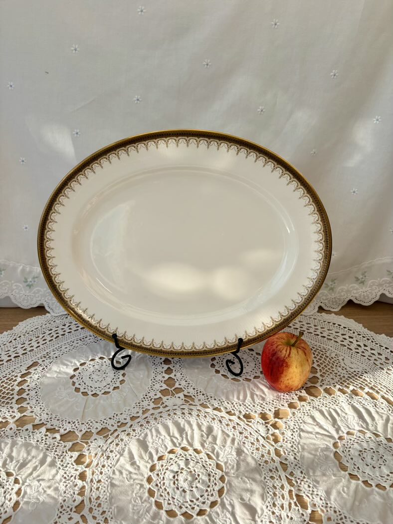 Decorative white plate with gold rim on a lace tablecloth with an apple beside it.