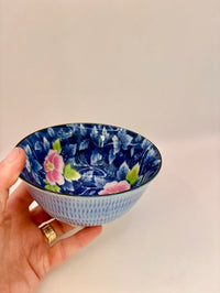 Hand holding a small decorative bowl with floral patterns on a plain background