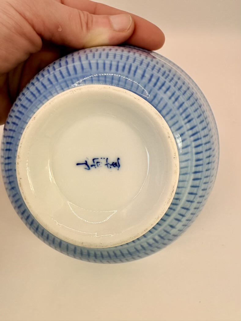 Ceramic bowl with blue interior and exterior design, held by a hand on a plain background