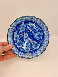Hand holding a blue decorative plate with floral patterns on a beige background