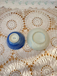 Two ceramic bowls, one blue and one white, on a lace tablecloth.