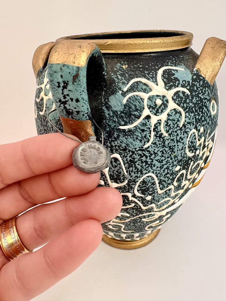 Ceramic vase with decorative patterns held by a hand against a neutral background