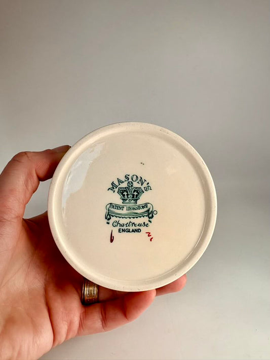 Hand holding a ceramic jar lid with branding on a plain background