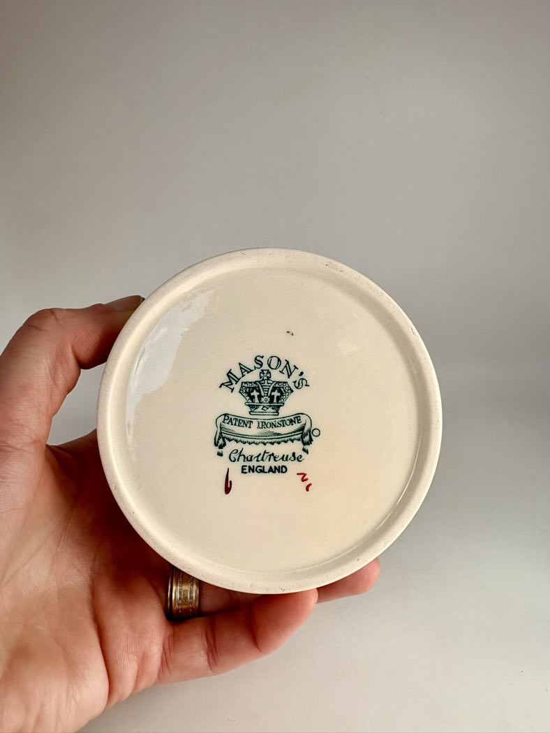 Hand holding a ceramic jar lid with branding on a plain background