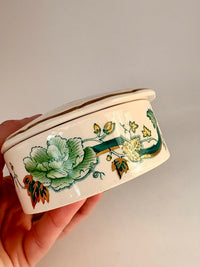 Hand holding a ceramic container with floral designs on a plain background