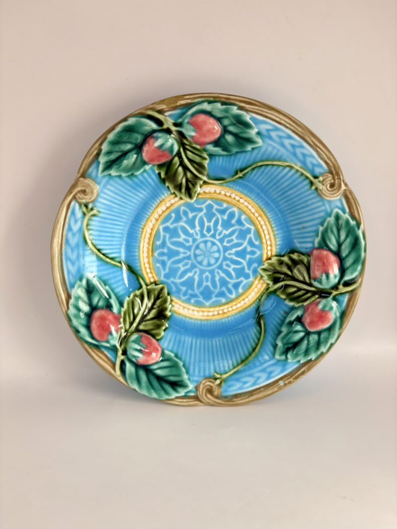 Decorative plate with blue background, gold center, green leaves, and red apples on a beige background