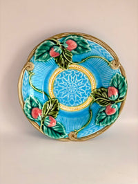 Decorative plate with blue background, gold center, green leaves, and red apples on a beige background